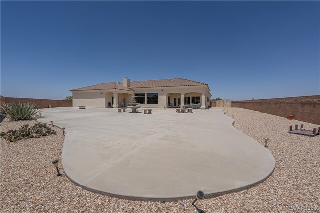 mediterranean / spanish home with a patio, a fenced backyard, a chimney, a tiled roof, and stucco siding