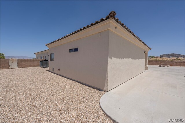 view of side of property with a tile roof, stucco siding, a patio area, fence, and central AC