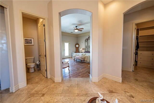 corridor with arched walkways, crown molding, and baseboards