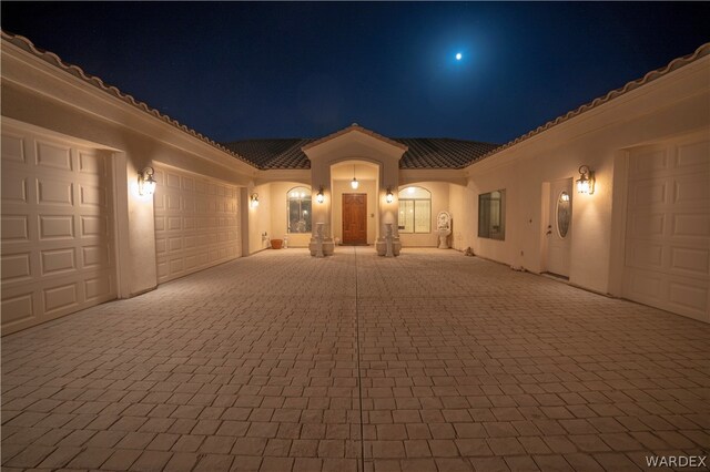 mediterranean / spanish-style home with an attached garage, a tiled roof, decorative driveway, and stucco siding