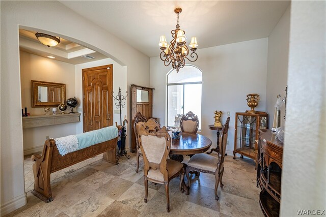 dining space featuring arched walkways, a raised ceiling, a notable chandelier, and baseboards