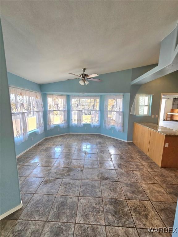 interior space featuring lofted ceiling, a textured ceiling, baseboards, and a ceiling fan