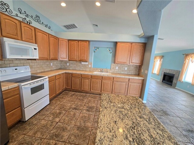 kitchen featuring white appliances, visible vents, backsplash, brown cabinets, and a tiled fireplace