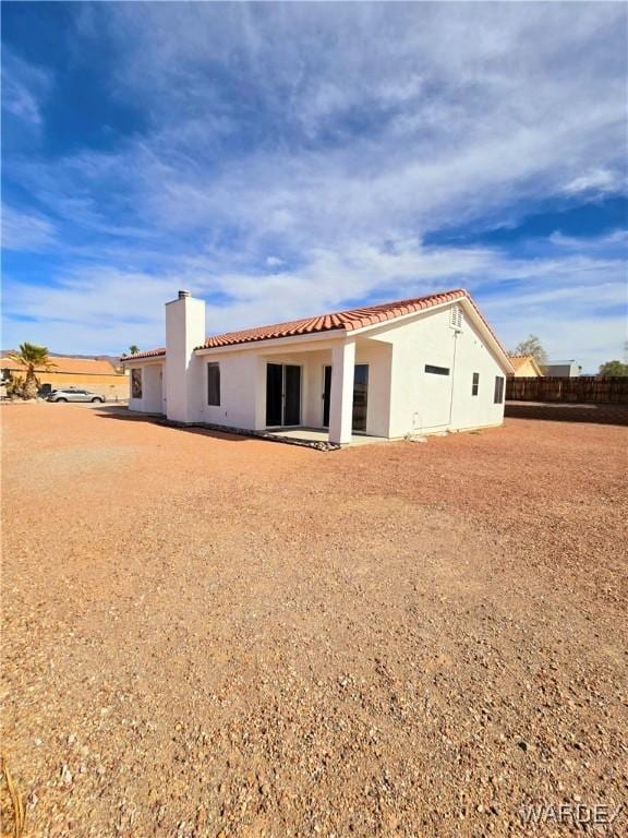 back of house with a tile roof, a chimney, and stucco siding