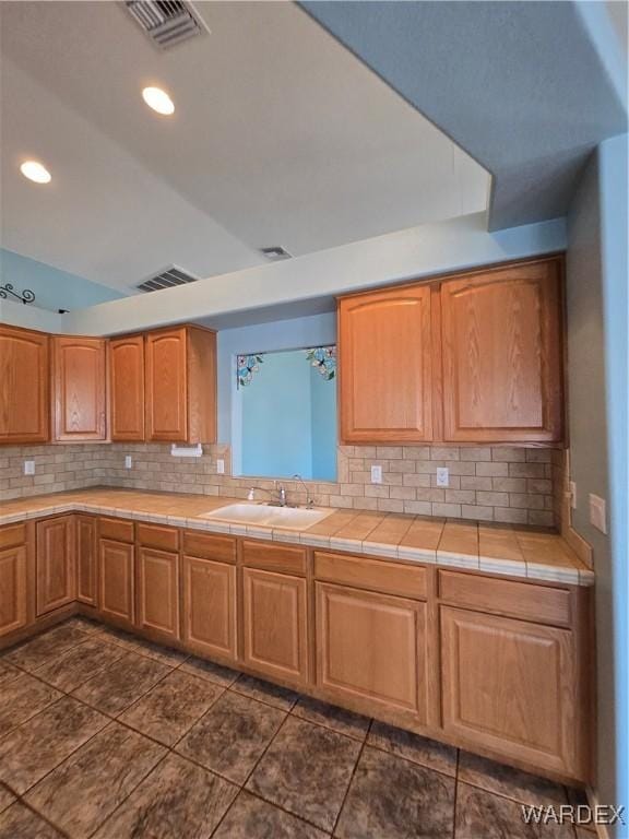 kitchen featuring tile countertops, tasteful backsplash, visible vents, brown cabinetry, and a sink