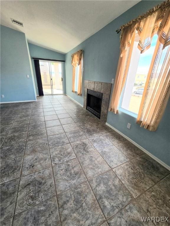 unfurnished living room with baseboards, visible vents, vaulted ceiling, and a tile fireplace