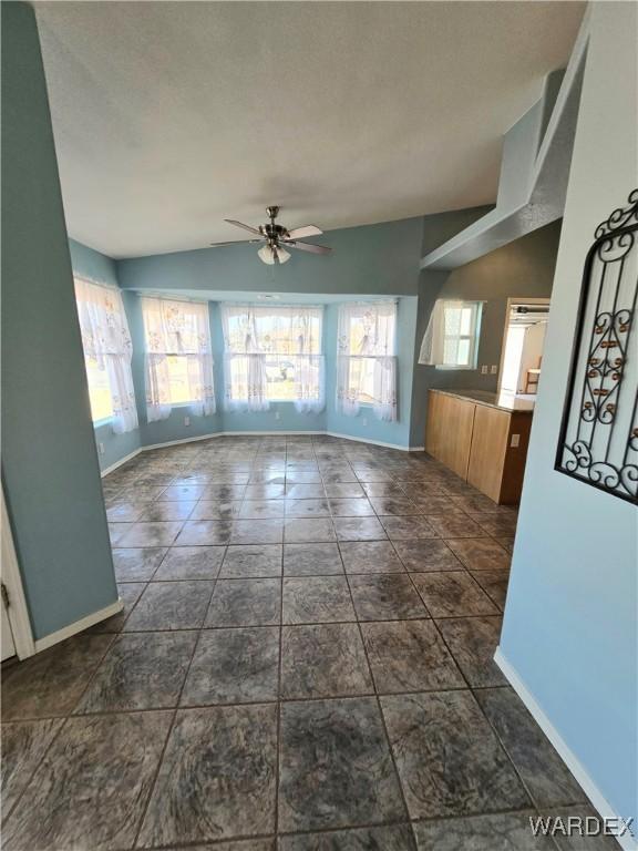 unfurnished living room with vaulted ceiling, ceiling fan, and baseboards