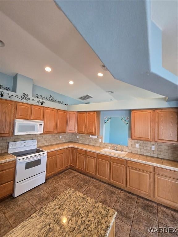 kitchen with white appliances, visible vents, brown cabinetry, and a sink