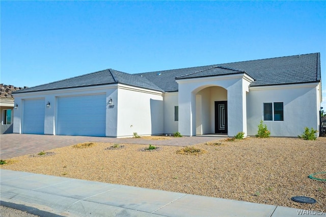 ranch-style house with a garage, a tiled roof, decorative driveway, and stucco siding