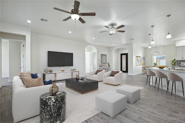 living room featuring light wood finished floors, visible vents, arched walkways, baseboards, and recessed lighting