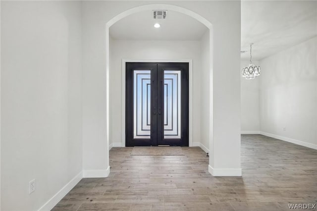 entrance foyer featuring light wood-style floors, baseboards, visible vents, and arched walkways