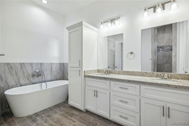 full bathroom featuring double vanity, wood tiled floor, a sink, a tile shower, and a freestanding tub