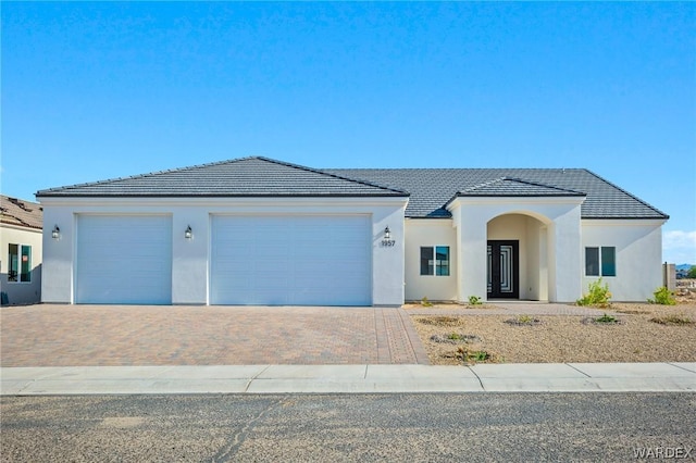 view of front facade featuring a garage, a tile roof, decorative driveway, and stucco siding