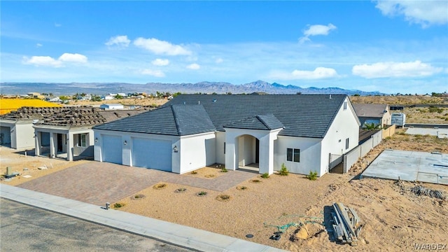 ranch-style house with an attached garage, a mountain view, a tiled roof, decorative driveway, and stucco siding