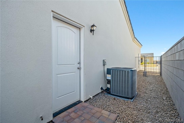 property entrance featuring fence, central AC, and stucco siding