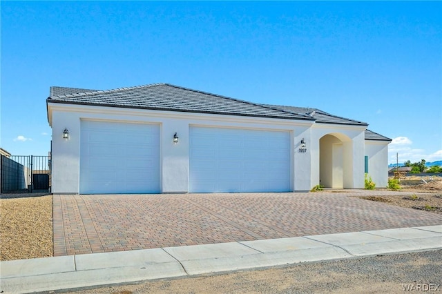 ranch-style house featuring a garage, a tiled roof, decorative driveway, and stucco siding