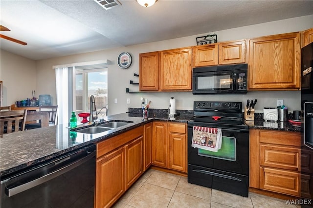 kitchen with brown cabinetry, dark stone countertops, a sink, and black appliances