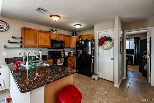 kitchen with visible vents, brown cabinets, a peninsula, black appliances, and a sink