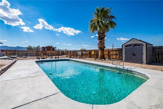 view of swimming pool with a storage shed, a fenced in pool, a fenced backyard, an outbuilding, and a mountain view