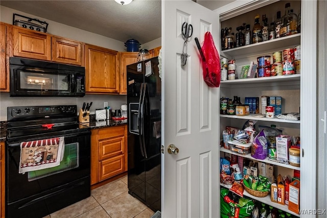 kitchen with light tile patterned flooring, open shelves, dark stone counters, black appliances, and brown cabinetry