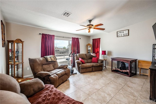 living room with a textured ceiling, light tile patterned flooring, visible vents, baseboards, and a ceiling fan