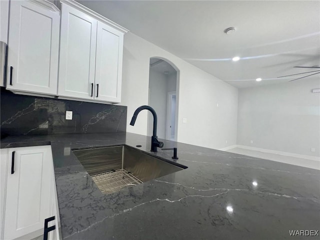 kitchen with tasteful backsplash, arched walkways, dark stone counters, white cabinetry, and a sink