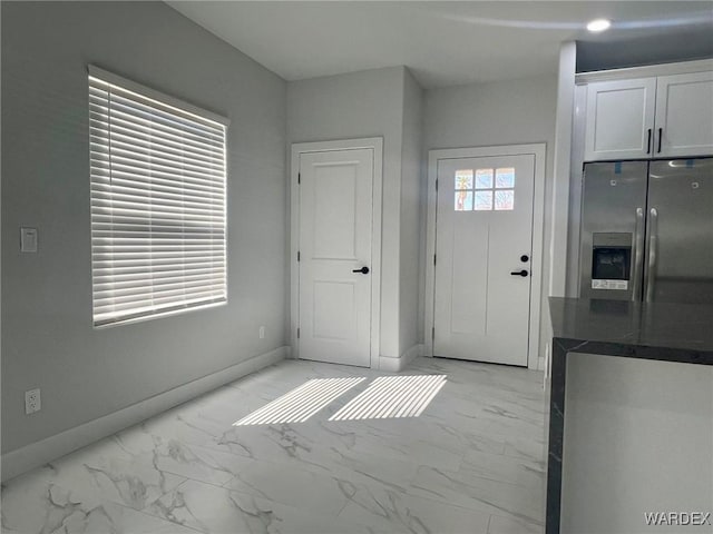 kitchen with dark countertops, white cabinets, stainless steel fridge, and marble finish floor