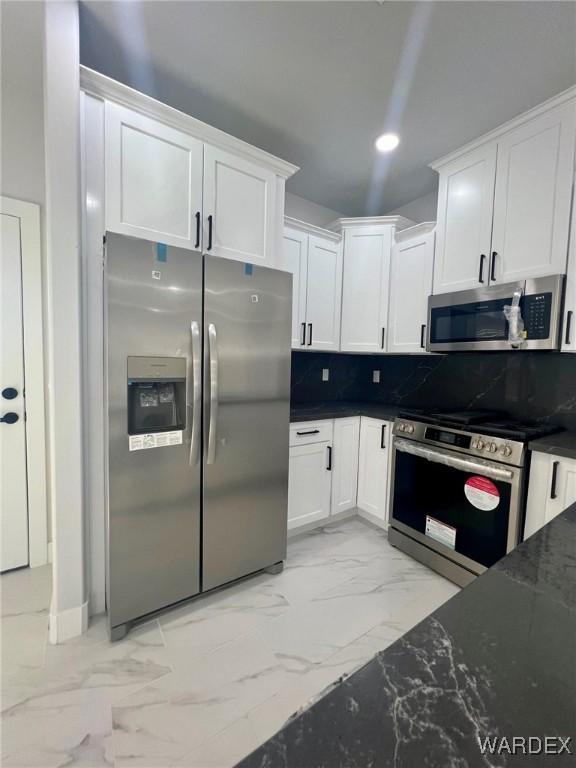 kitchen with stainless steel appliances, white cabinets, marble finish floor, backsplash, and dark stone countertops