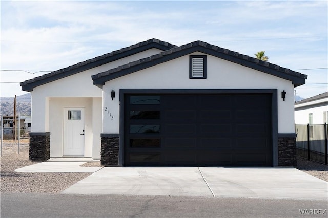 view of front of property featuring stone siding, concrete driveway, fence, and stucco siding