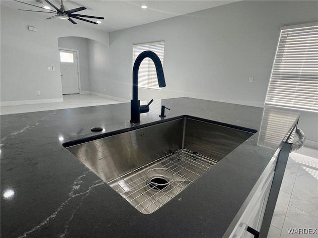 details featuring dark stone counters, a sink, arched walkways, and ceiling fan