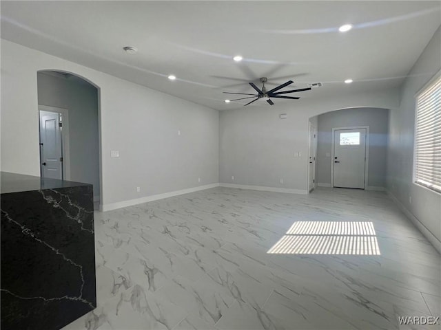 unfurnished living room with arched walkways, marble finish floor, baseboards, and recessed lighting