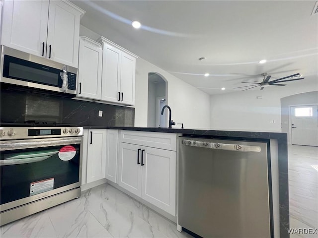 kitchen with white cabinetry, marble finish floor, appliances with stainless steel finishes, decorative backsplash, and dark countertops