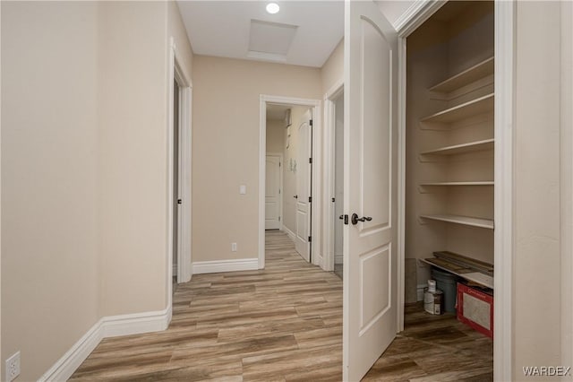 hall with light wood-type flooring, attic access, and baseboards