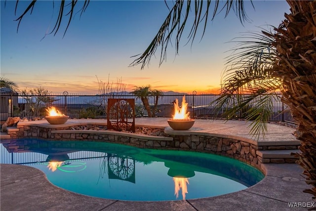 pool at dusk featuring a fire pit, a patio area, and fence