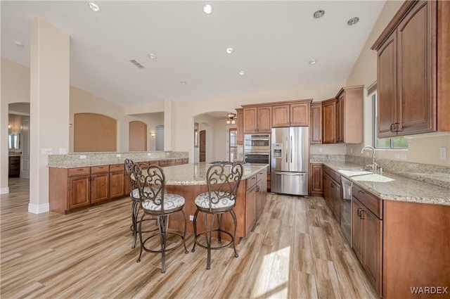 kitchen featuring a sink, vaulted ceiling, appliances with stainless steel finishes, a center island, and a kitchen bar