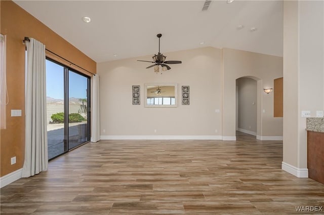 spare room featuring arched walkways, light wood finished floors, and vaulted ceiling