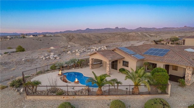 pool at dusk featuring a patio, a fenced backyard, a mountain view, and a fenced in pool