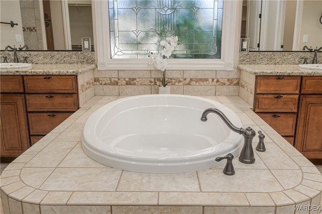 full bath with two vanities, a garden tub, and a sink