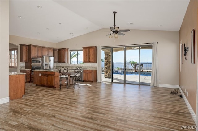 kitchen with light wood-style flooring, a kitchen island, open floor plan, brown cabinetry, and stainless steel fridge