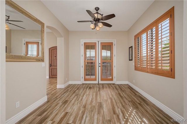 spare room with arched walkways, french doors, a ceiling fan, wood finished floors, and baseboards