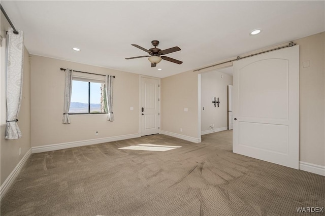 empty room with baseboards, a barn door, recessed lighting, and light colored carpet