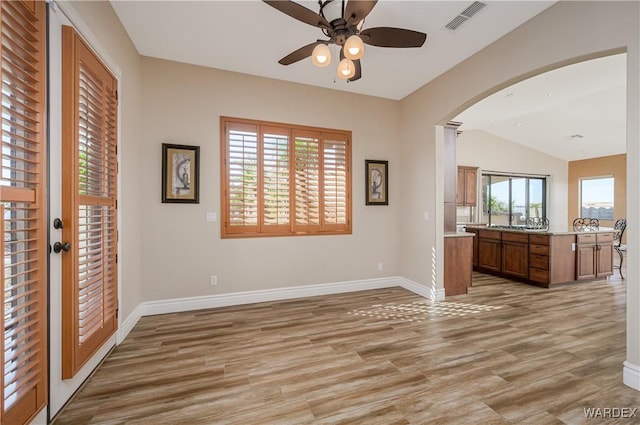 interior space featuring light wood-style flooring, visible vents, arched walkways, and baseboards