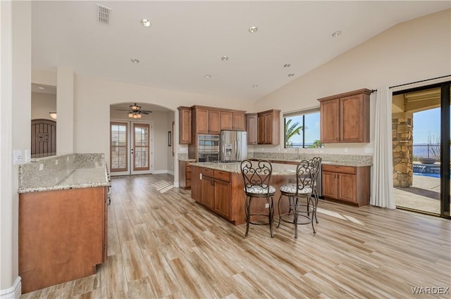 kitchen featuring arched walkways, appliances with stainless steel finishes, a kitchen island, and brown cabinets