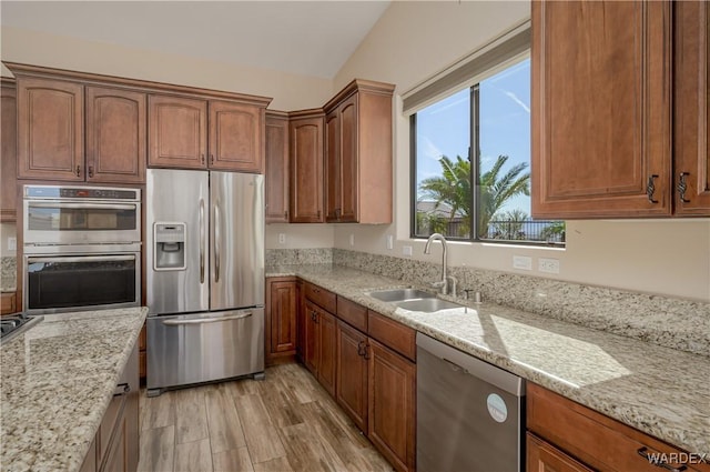 kitchen with light stone counters, brown cabinets, stainless steel appliances, light wood-style floors, and a sink