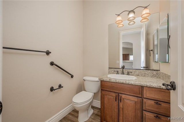 half bathroom featuring baseboards, vanity, toilet, and wood finished floors