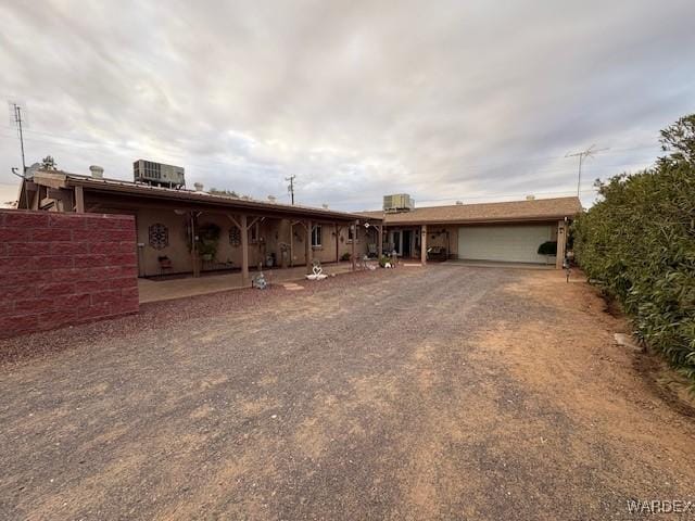 ranch-style home with central air condition unit, a garage, and dirt driveway