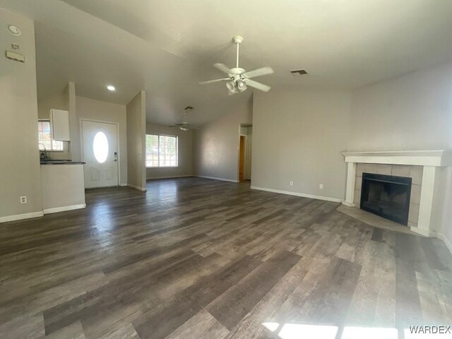 unfurnished living room with baseboards, visible vents, a tile fireplace, dark wood-style flooring, and vaulted ceiling