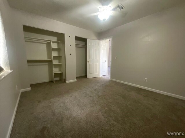 unfurnished bedroom featuring baseboards, visible vents, dark colored carpet, and multiple closets