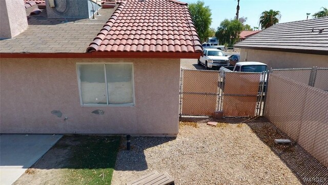 view of property exterior featuring a tile roof, a gate, fence, and stucco siding