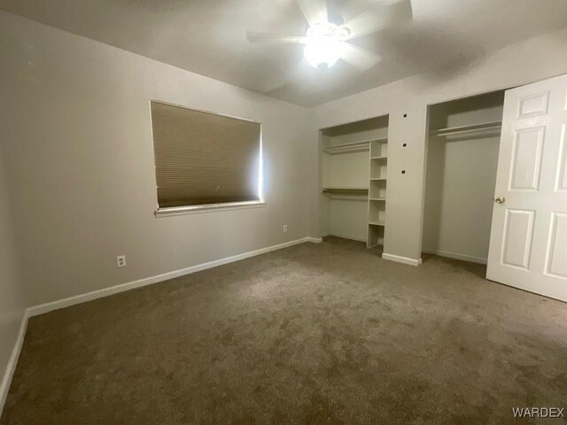 unfurnished bedroom with a ceiling fan, baseboards, dark colored carpet, and two closets